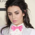 Charli XCX wears her black hair swept back in bouffant style with grey and pink suit jacket at 57th Annual Grammy Awards