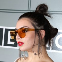 Charli XCX wears her dark tresses in twin bun hairstyle with loose strands falling around her face worn with red sunglasses