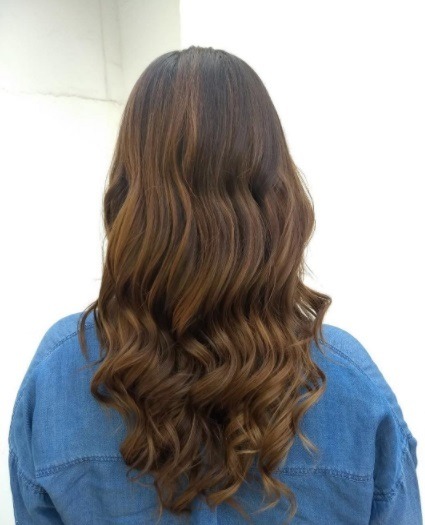 Balayage long hair: back shot of a woman with long curly balayage brunette hair with highlights