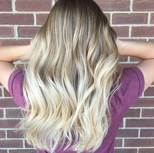 Balayage long hair: Back view of a woman running her hands through her creamy blonde balayage long hair