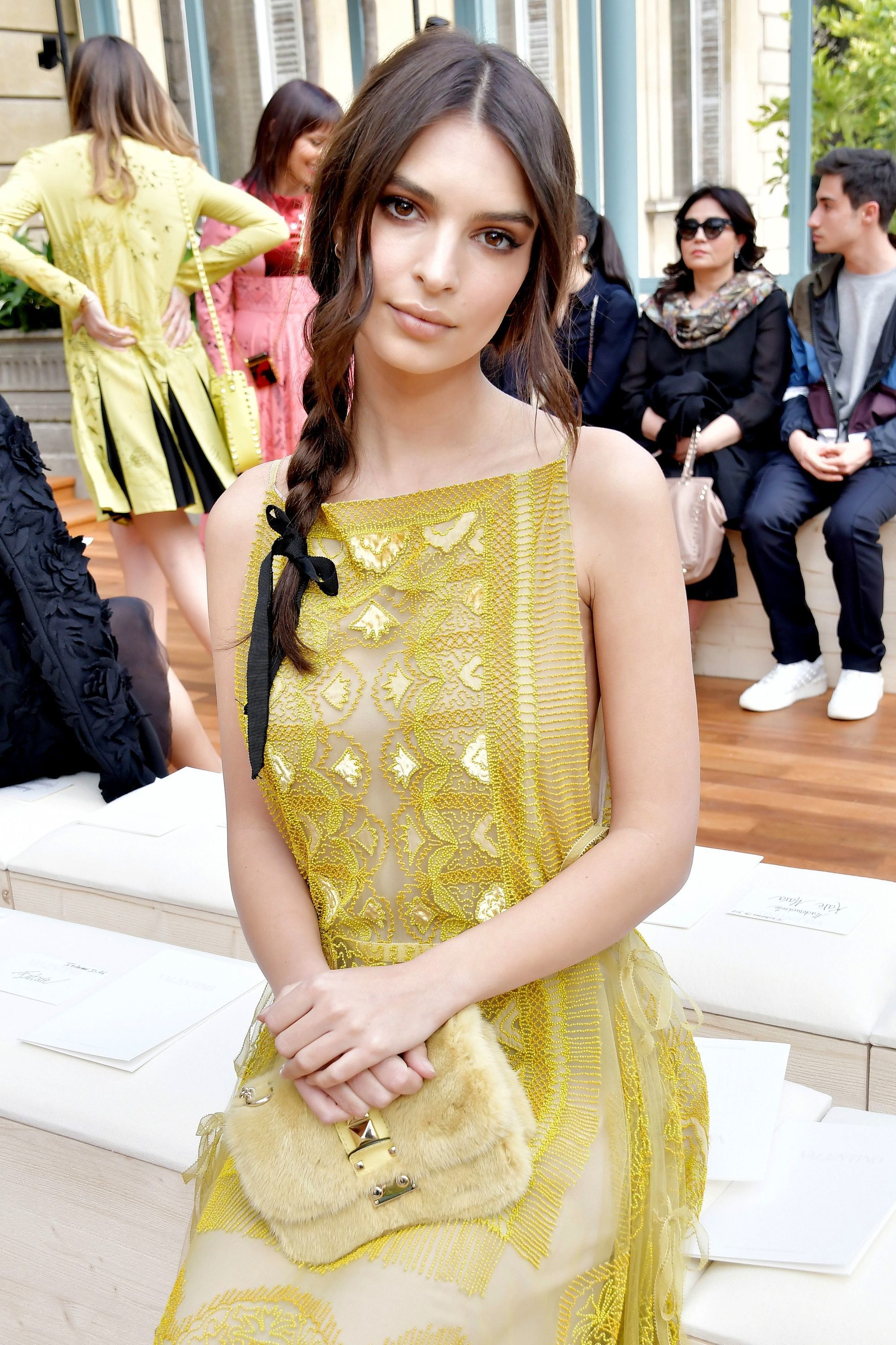 Emily Ratajkowski long brown hair in side braid with ribbon at end of braid at fashion show