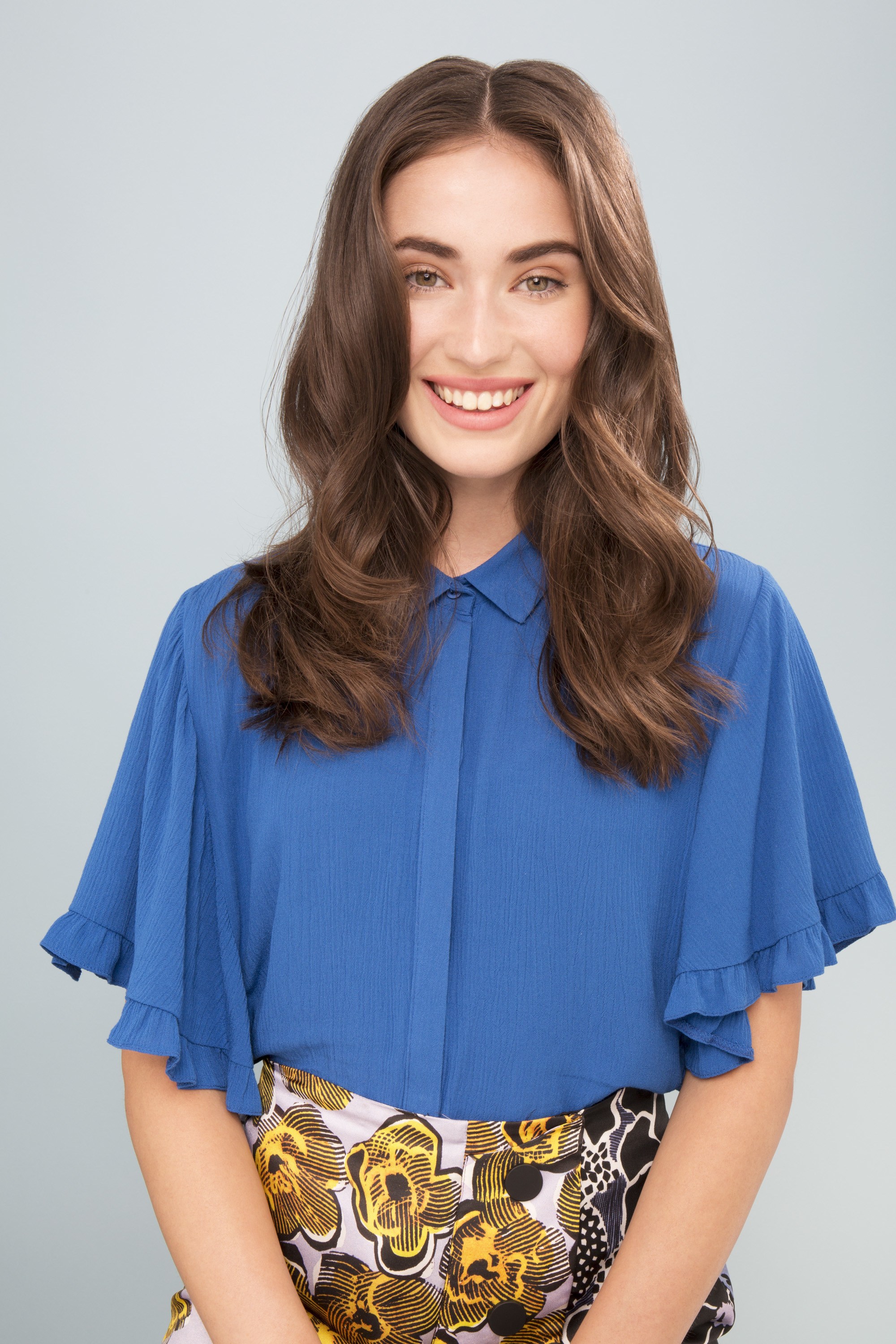 Best hair serum for dry hair: Model with wavy brown medium length hair wearing a blue blouse with pattern trousers.