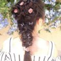 Brown long hair in flower braid style and french braid with pink flowers inserted into the braids
