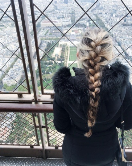 woman with long blonde hair looking out from the eiffel tower with her hair in a french braid