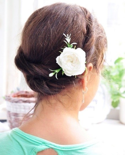 back view of a woman with brunette hair in a milkmaid twist hairstyle with a pink flower hair accessory