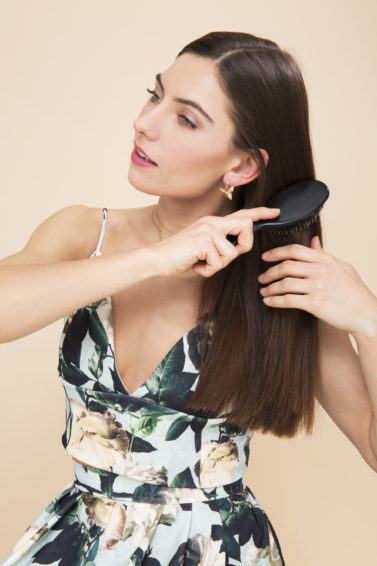 Keratin shampoo: Model brushing her long straight brown hair wearing a floral outfit.