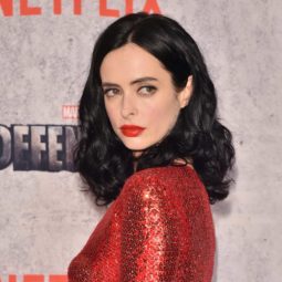 Krysten Ritter wears her black mid length tresses in loose curls hairstyle and bol red lipstick and red sequin cut out dress