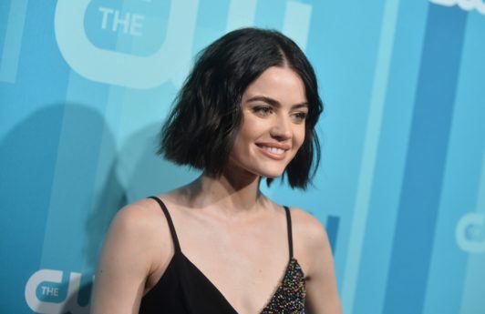 lucy hale with with wavy black hair on the red carpet smiling