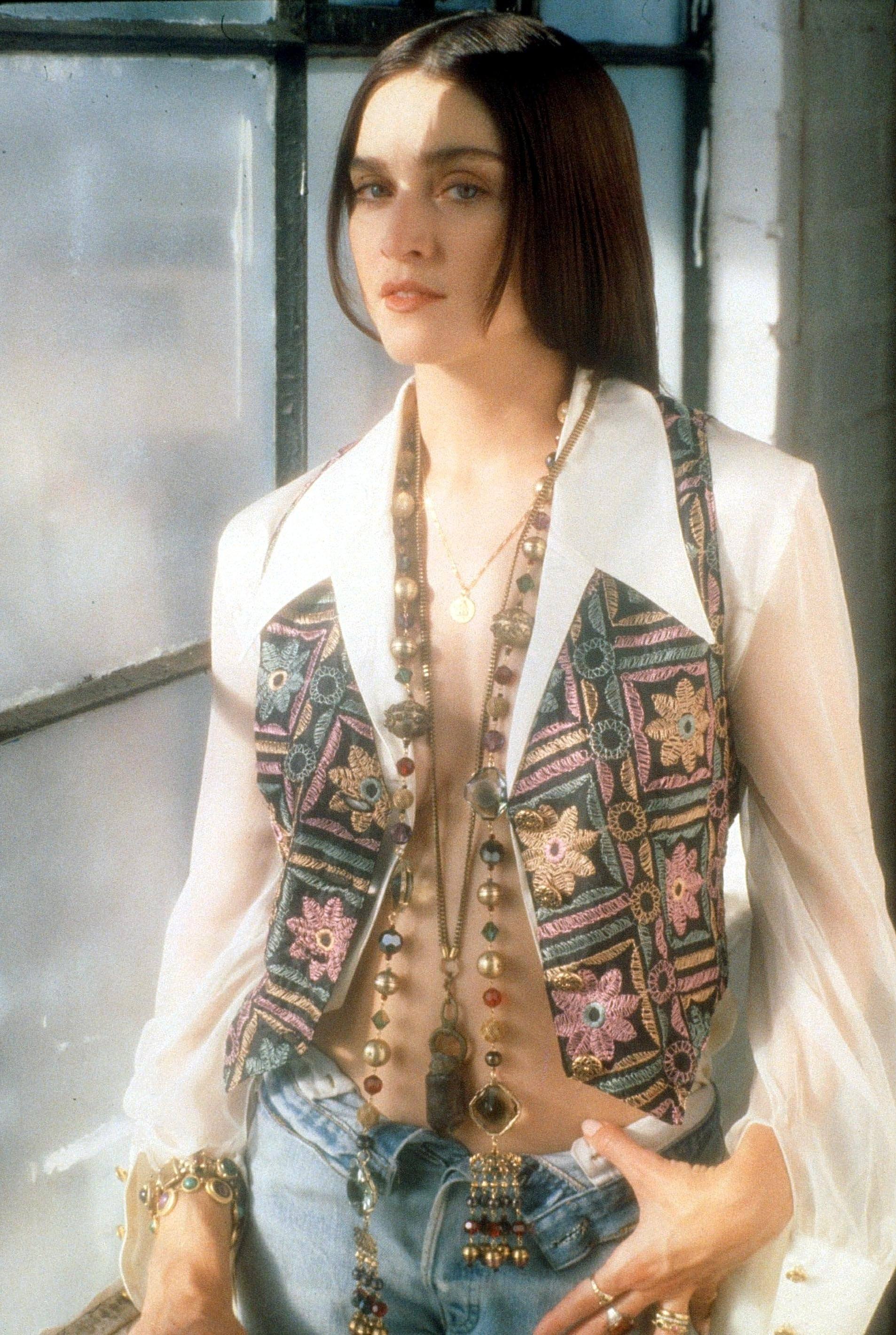 Madonna in 1989 with long brunette hair wearing a white blouse with patterned waistcoat and long beads