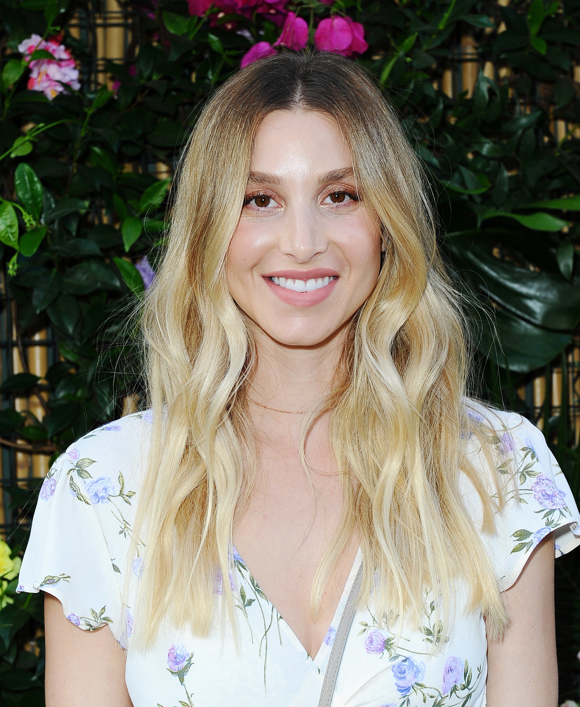 Whiteny Port shows off her long blonde hair in a centre part wavy style wearing a floral v neck dress
