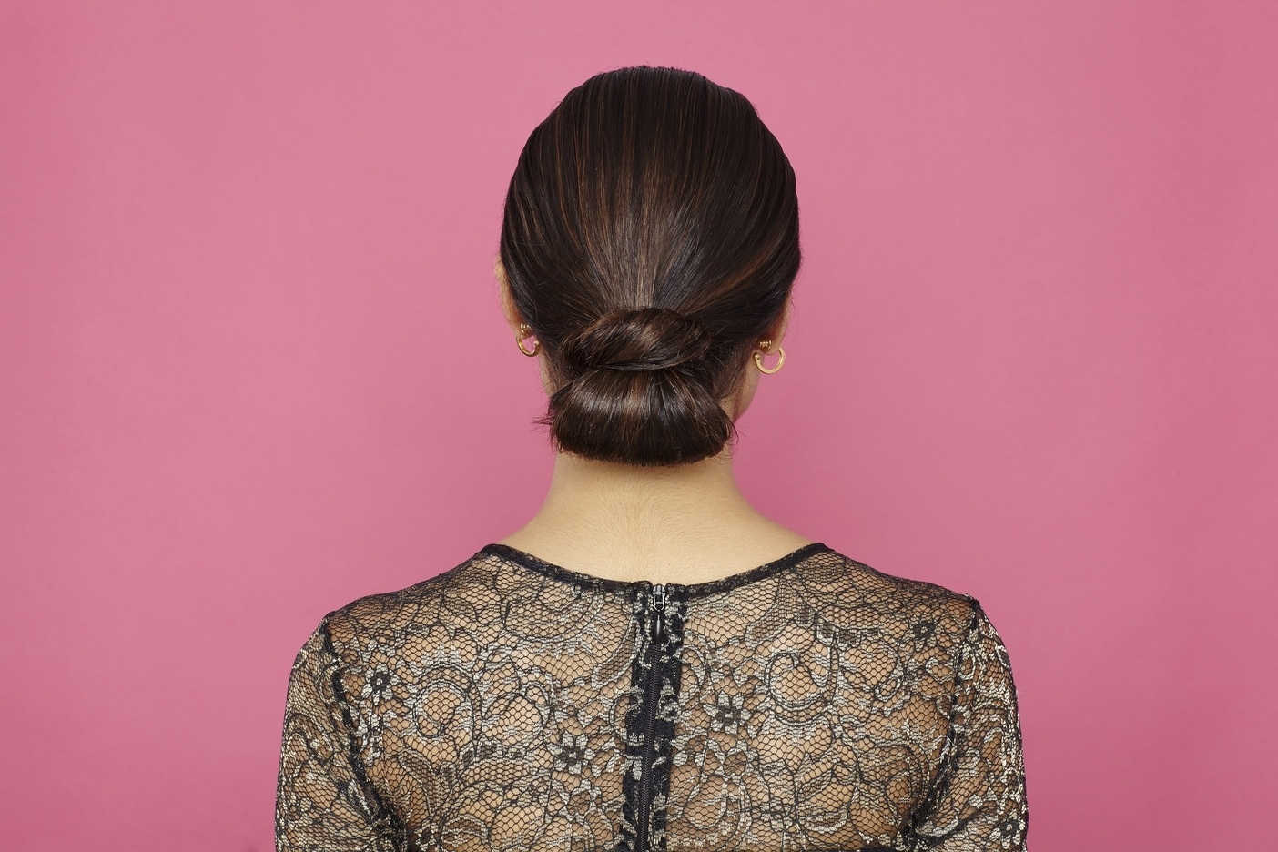 brown hair model showing of low sleek wrapped tuck bun hairstyle from back view