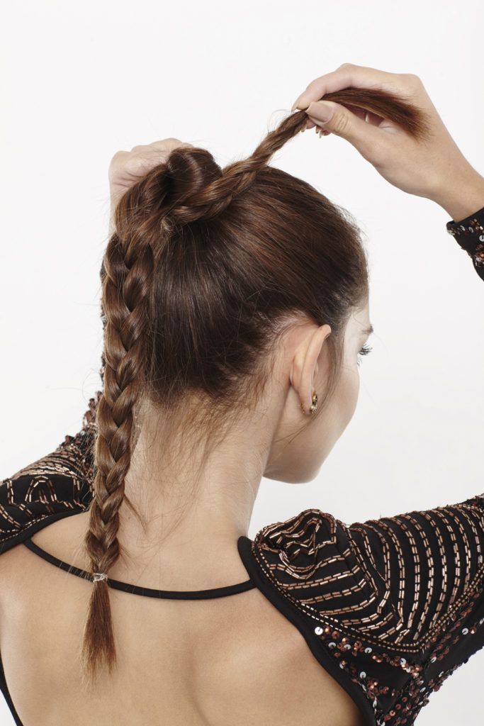 woman with brunette hair wrapping a braided ponytail into a bun