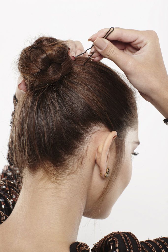 woman with brunette hair pinning her braided bun in place