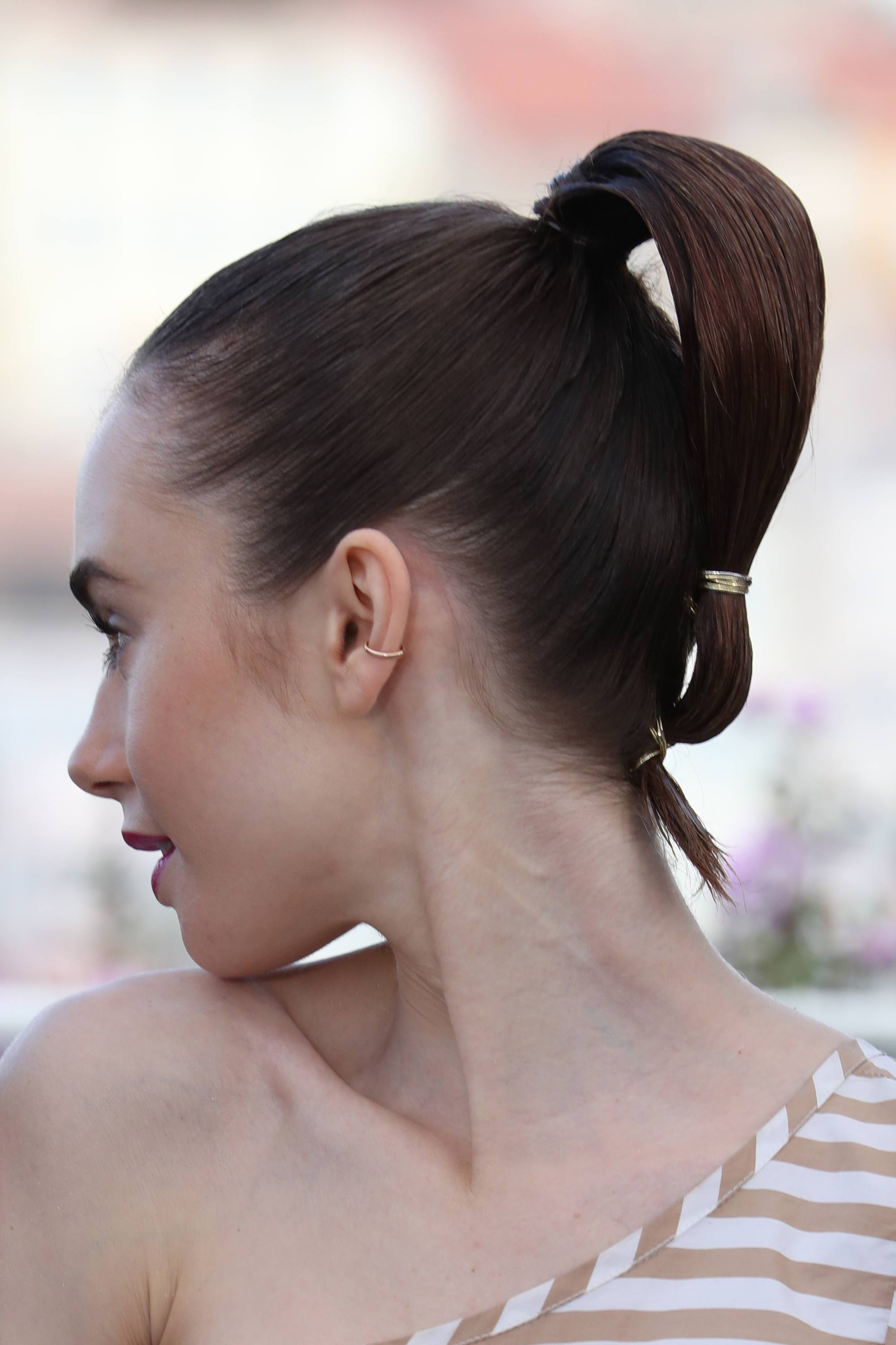 short hairstyles for school: lily collins with sleek looped ponytail with gold wrapping on it