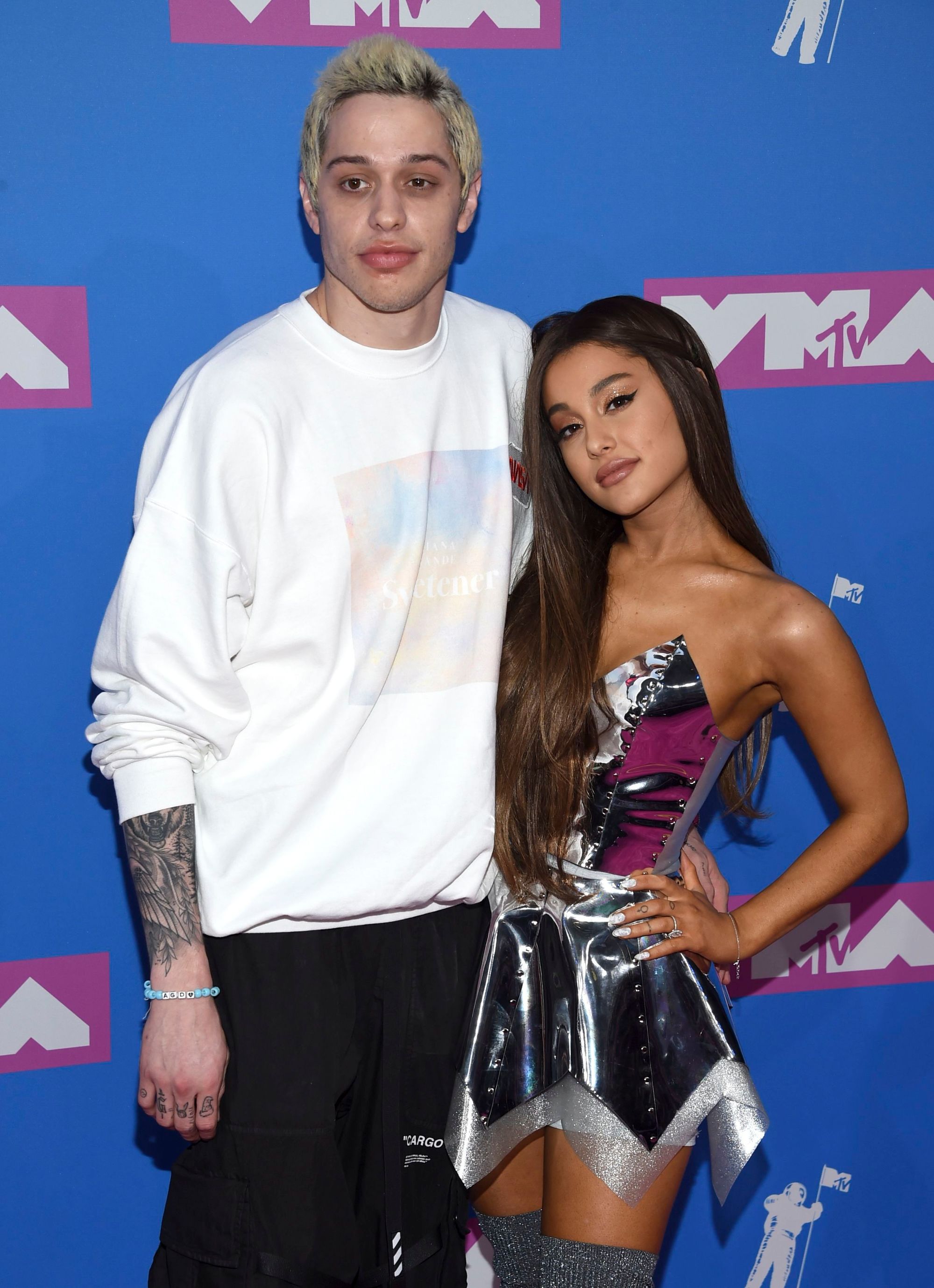 Red carpet hairstyles: Ariana Grande with long caramel brown hair with a simple twist in it, standing next to Pete Davidson on the VMA red carpet.