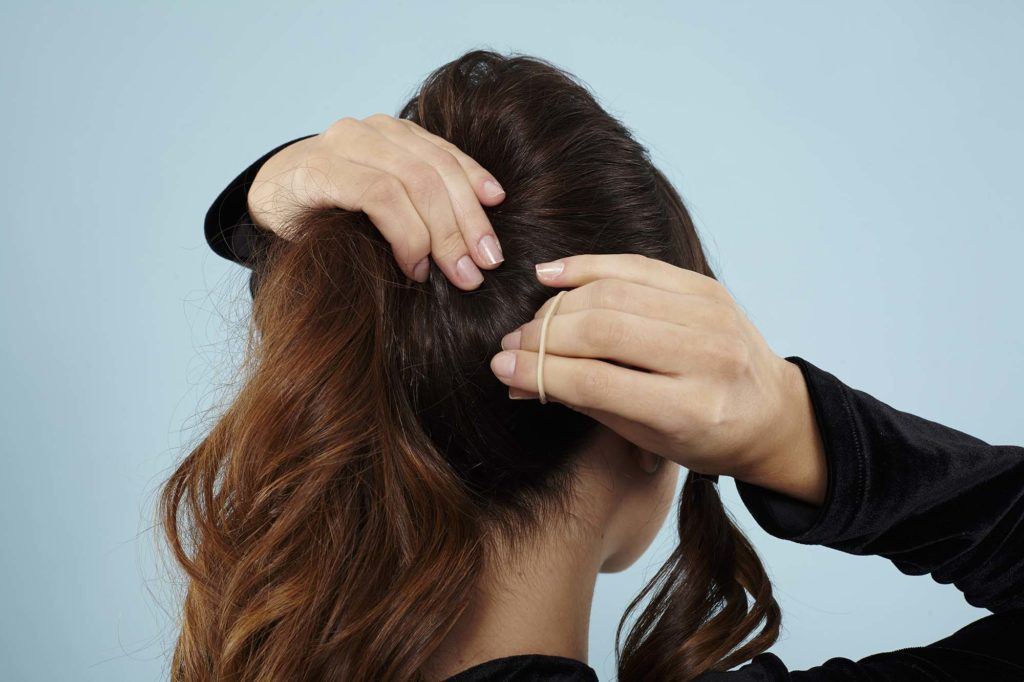 Curly ponytail tutorial: Back view of a brunette model creating her ponytail
