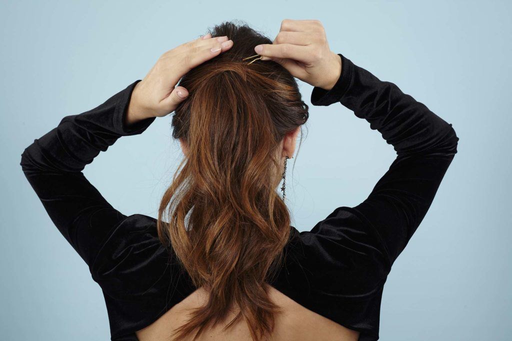 Curly ponytail tutorial: Back view of a brunette model pinning her ponytail
