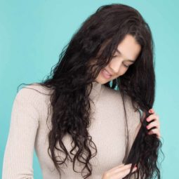 model with long dark brown curly hair looking at ends of hair