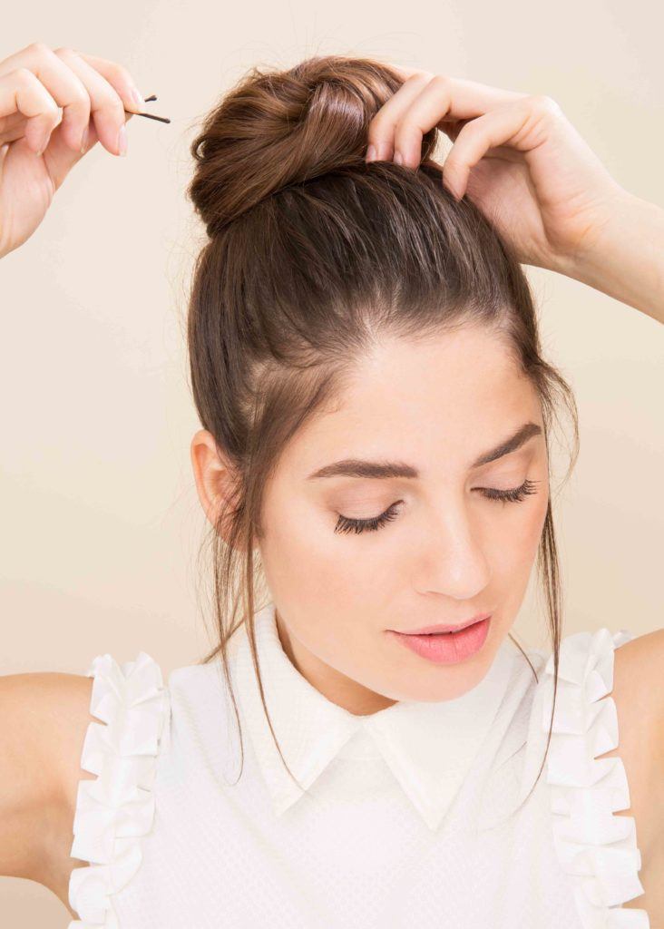 Woman with brunette hair in a topknot bun adding bobby pins