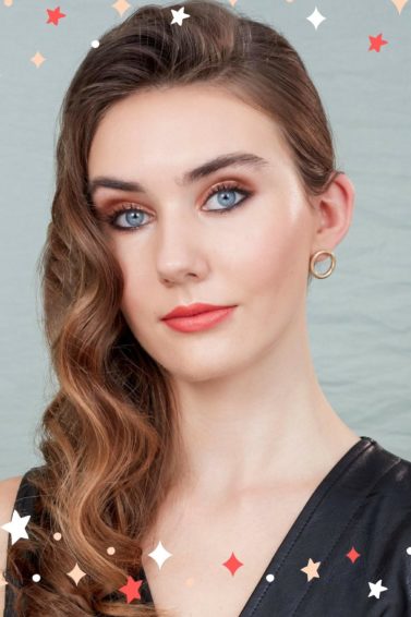 Party hair tips: Woman with chestnut brown glam hollywood curls, wearing black and posing against a grey background in a studio setting