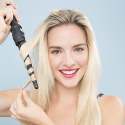 blonde model with long hair using a curling wand to curl her hair