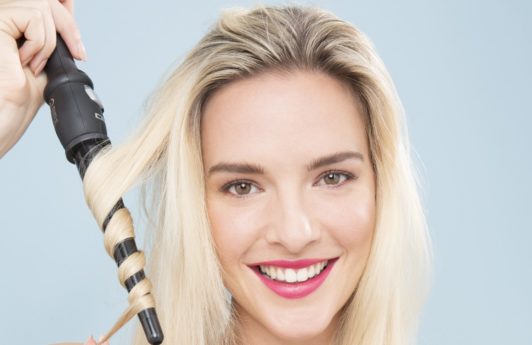blonde model with long hair using a curling wand to curl her hair