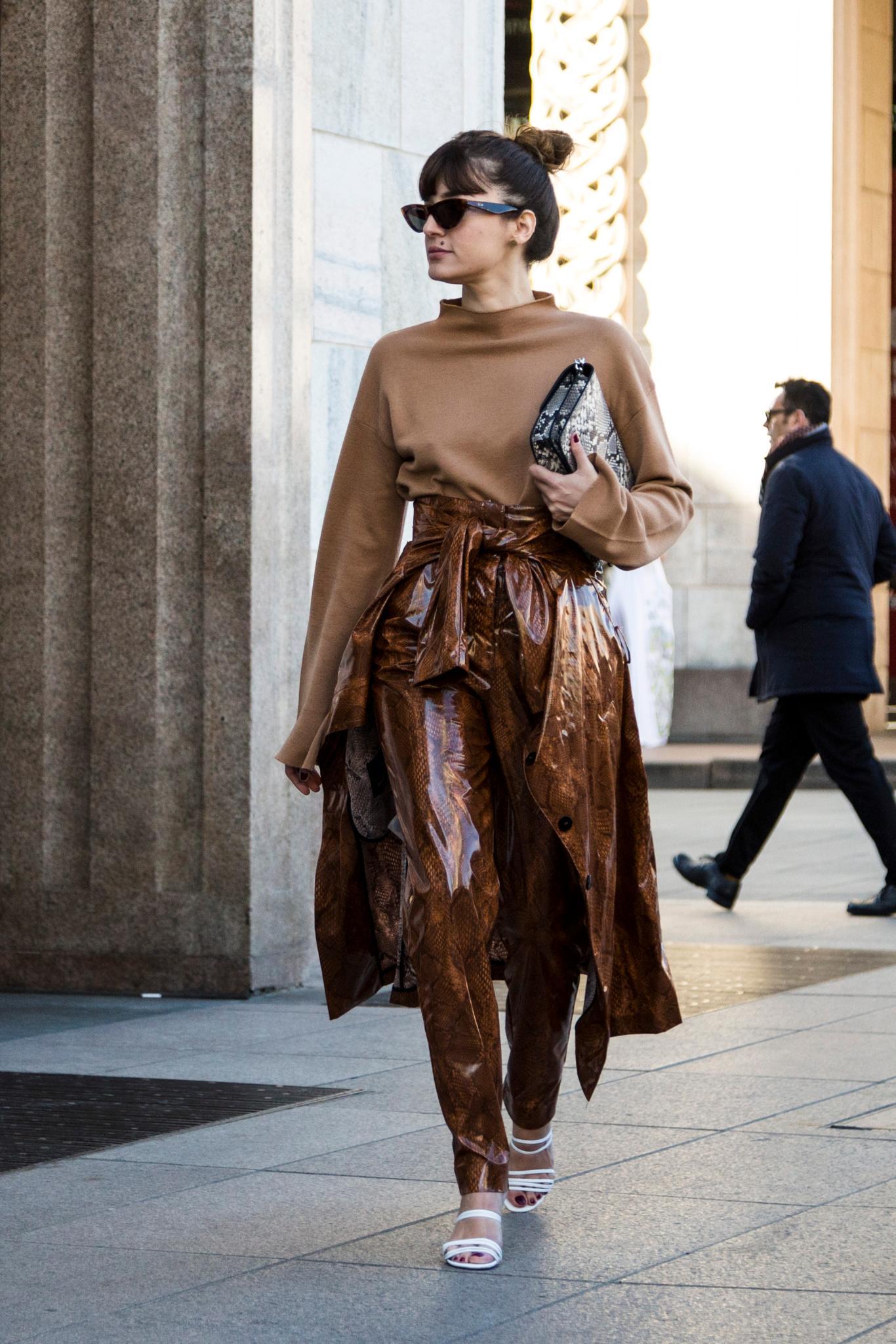 Milan Fashion Week Street Style: Woman with dark brown hair in high messy bun with full fringe bangs wearing all brown outfit holding a clutch bag.
