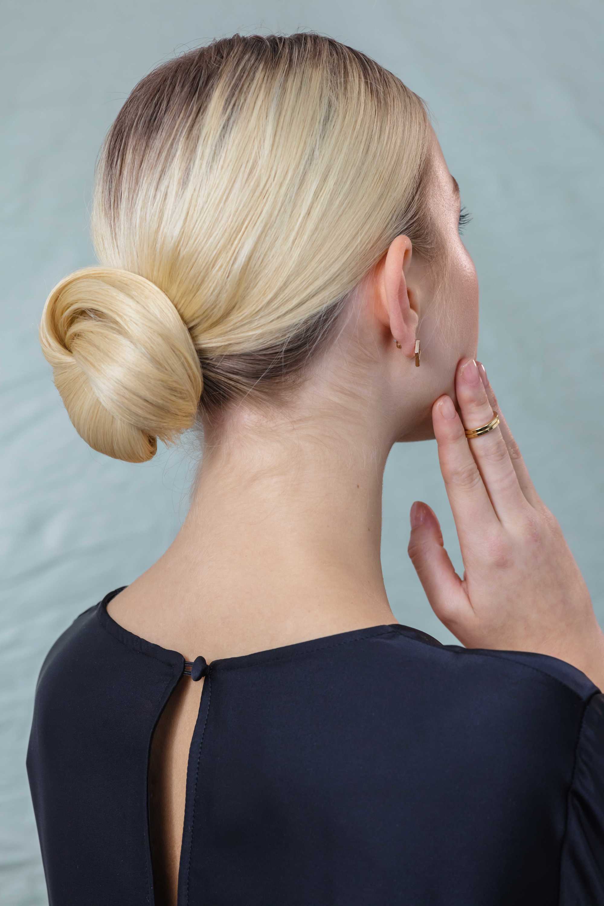 Back shot of woman with golden blonde hair styled into a polished, low chignon, wearing blue dress and posing in a studio setting