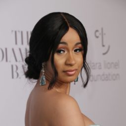 Cardi B looking over shoulder with black hair in low updo with loose strands framing the face wearing strapless blue dress
