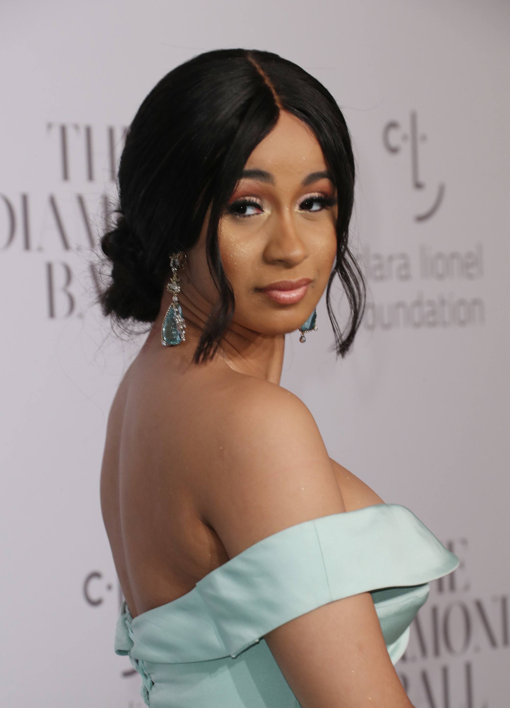 Cardi B looking over shoulder with black hair in low updo with loose strands framing the face wearing strapless blue dress