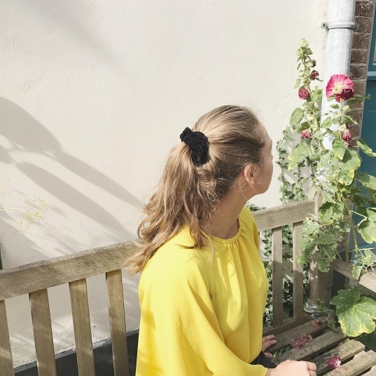 back view of a woman wearing a yellow top with her blonde hair in a scrunchie