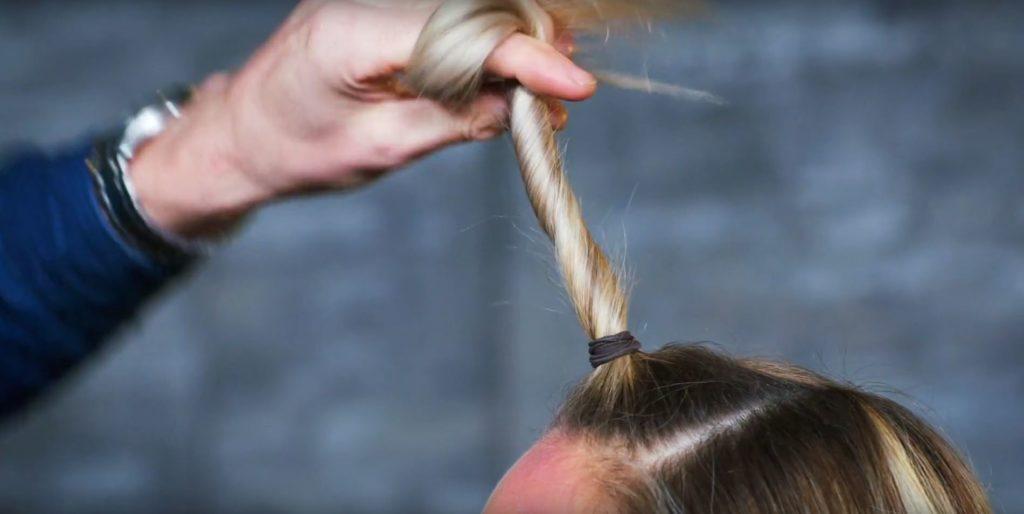 Unicorn Halloween tutorial: Close-up shot of a stylist twisting a section of a blonde model's hair into a unicorn horn for Halloween.