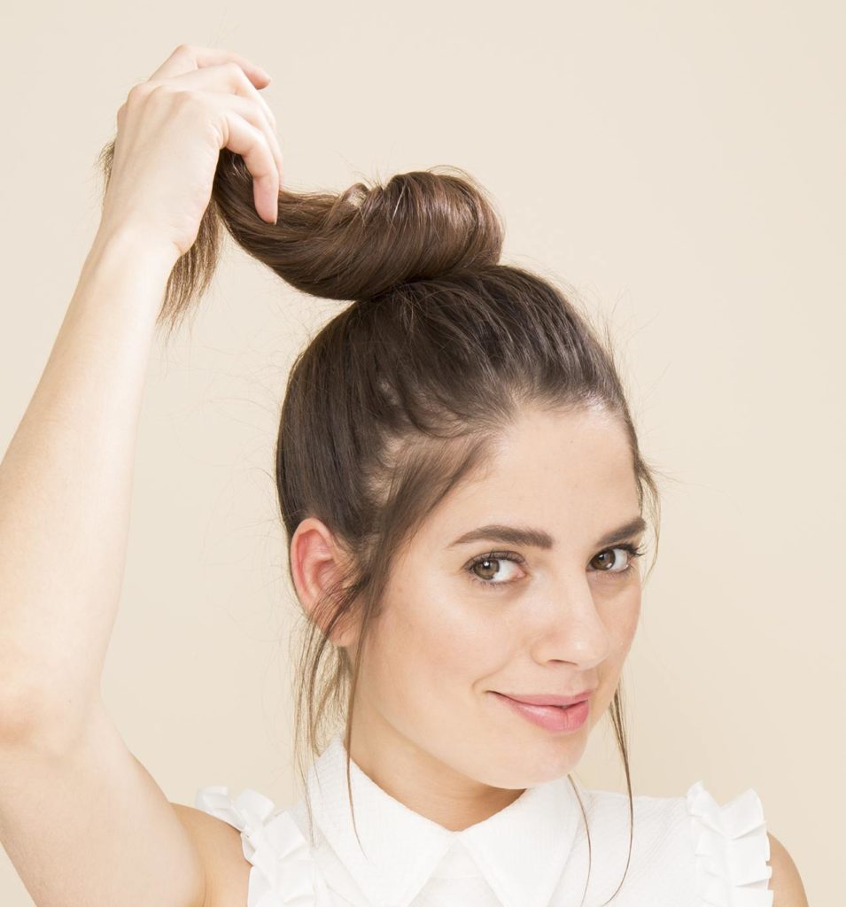 Woman with brunette hair in a ponytail twisting it to make a topknot bun