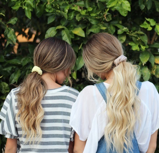 back view of two women with their long hair in ponytails tied with scrunchies