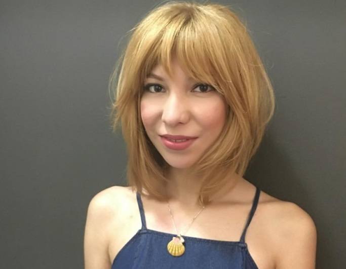 woman with a line with bangs hairstyle wearing blue denim dress and pearl necklace