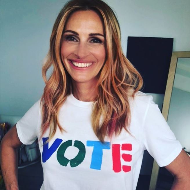 Fall hair colours: Julia Roberts with wavy medium length blonde hair with subtle pink highlights wearing a white tshirt with a slogan saying vote.