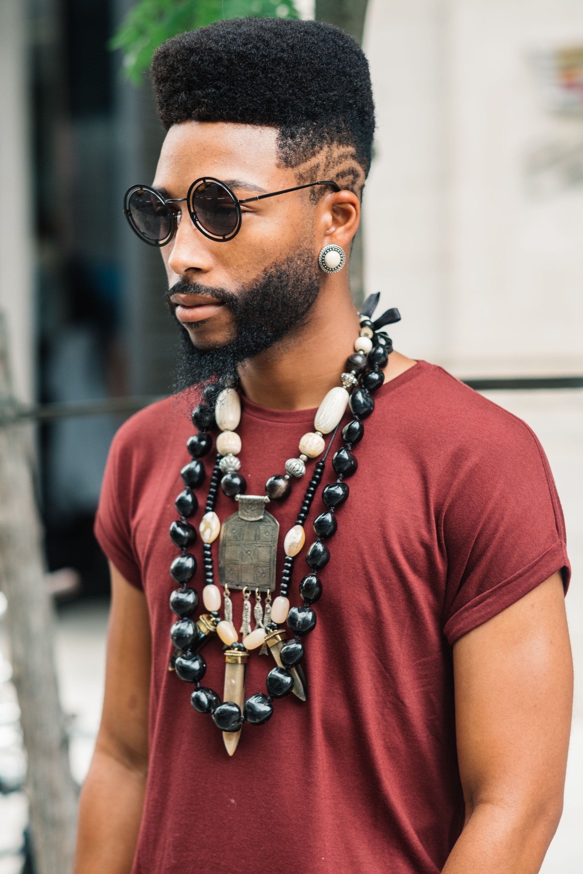 Vintage hairstyles for men: Street style shot of a man with an afro high top with a low fade hairstyle, wearing a red top and necklaces