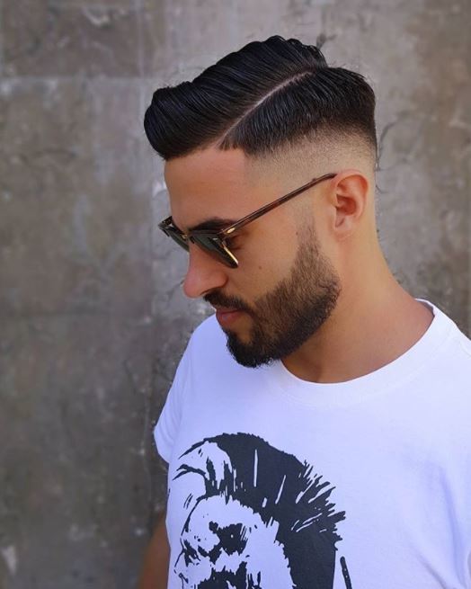 side shot of a man with dark hair in a side comb fade hairstyles wearing sunglasses and a white t-shirt