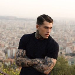 shot of a mane with dark hair in a longer side comb fade and tattoos on his arms