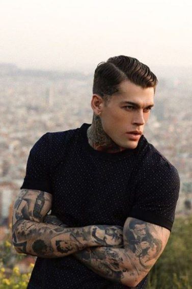 shot of a mane with dark hair in a longer side comb fade and tattoos on his arms