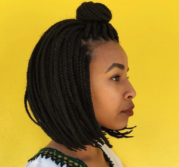 Box braids bob: Woman with dark brown half up half down short bob box braids, with yellow background