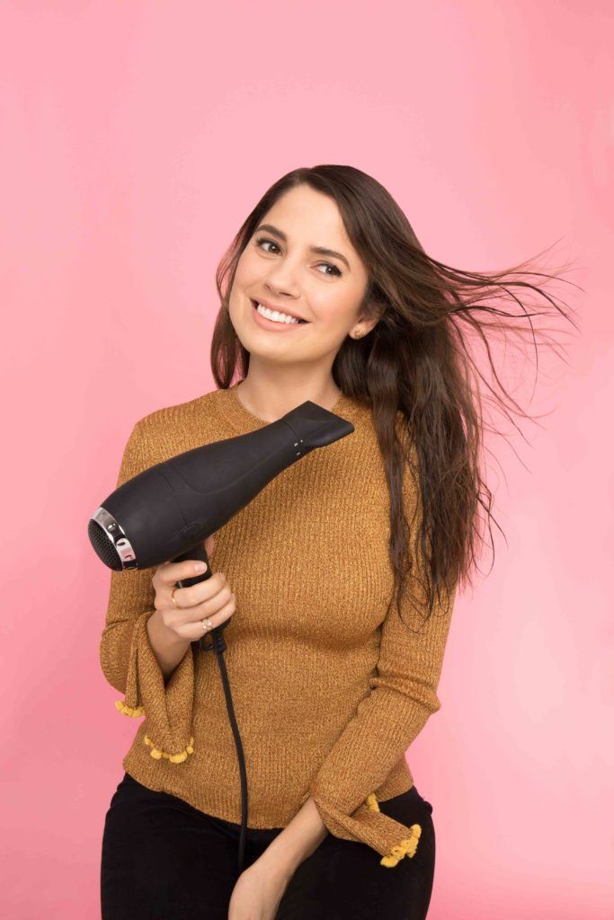 model blow drying her hair in studio smiling