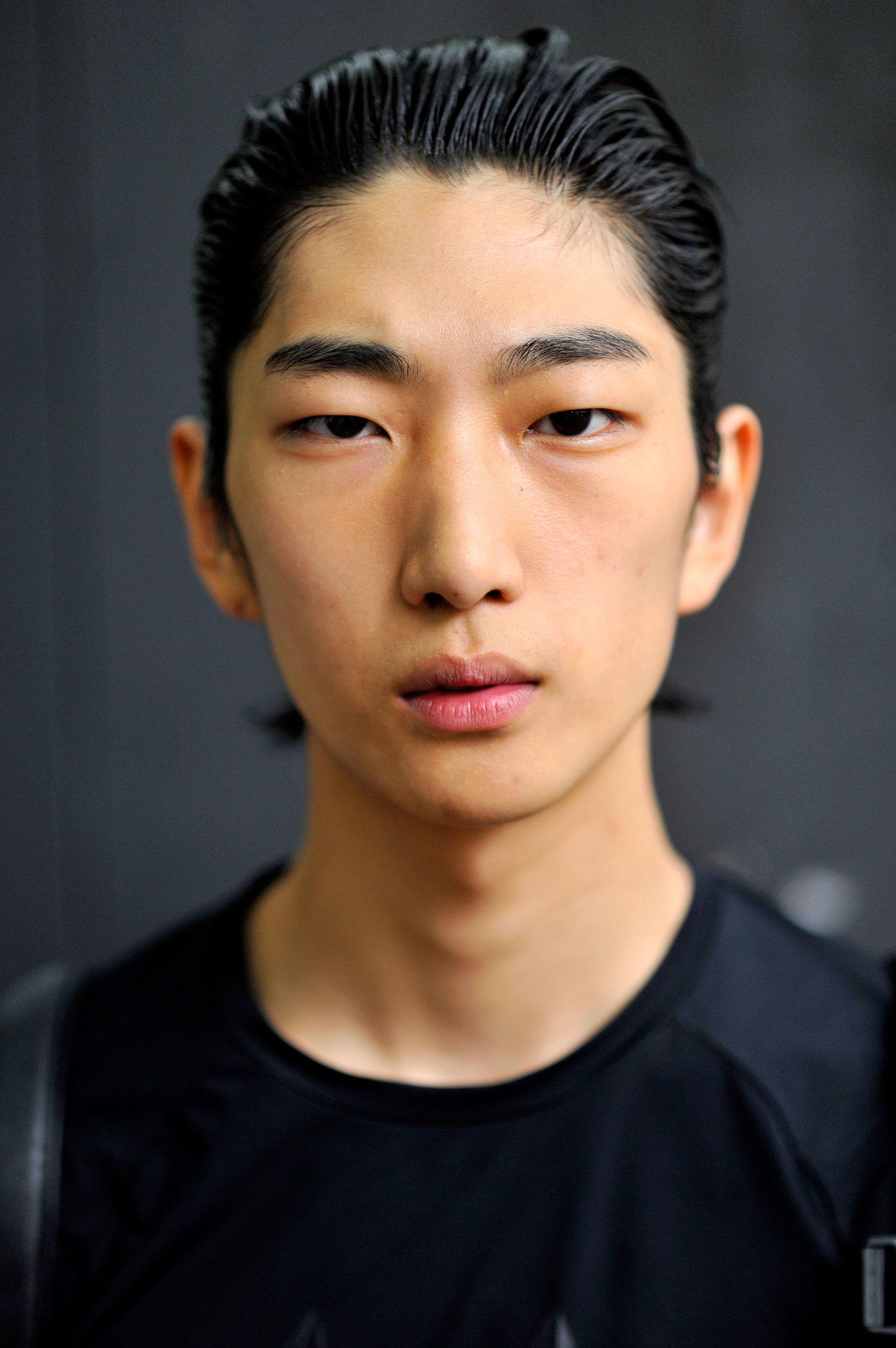 Vintage hairstyles for men: Street style up shot of a man with slicked back dark hair, wearing black and posing