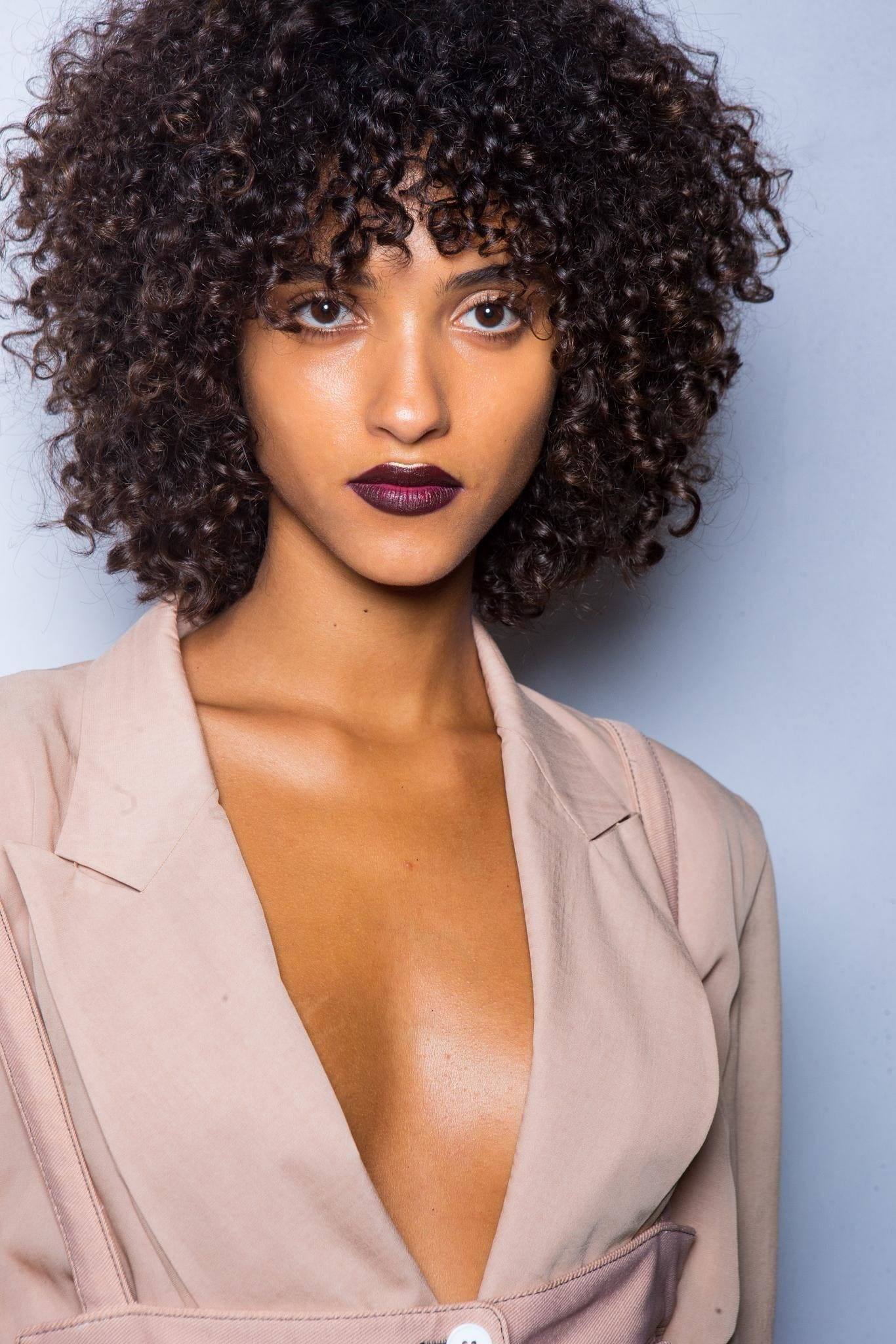 curly hair type quiz: backstage shot of model with curly hair, wearing suit and dark lipstick