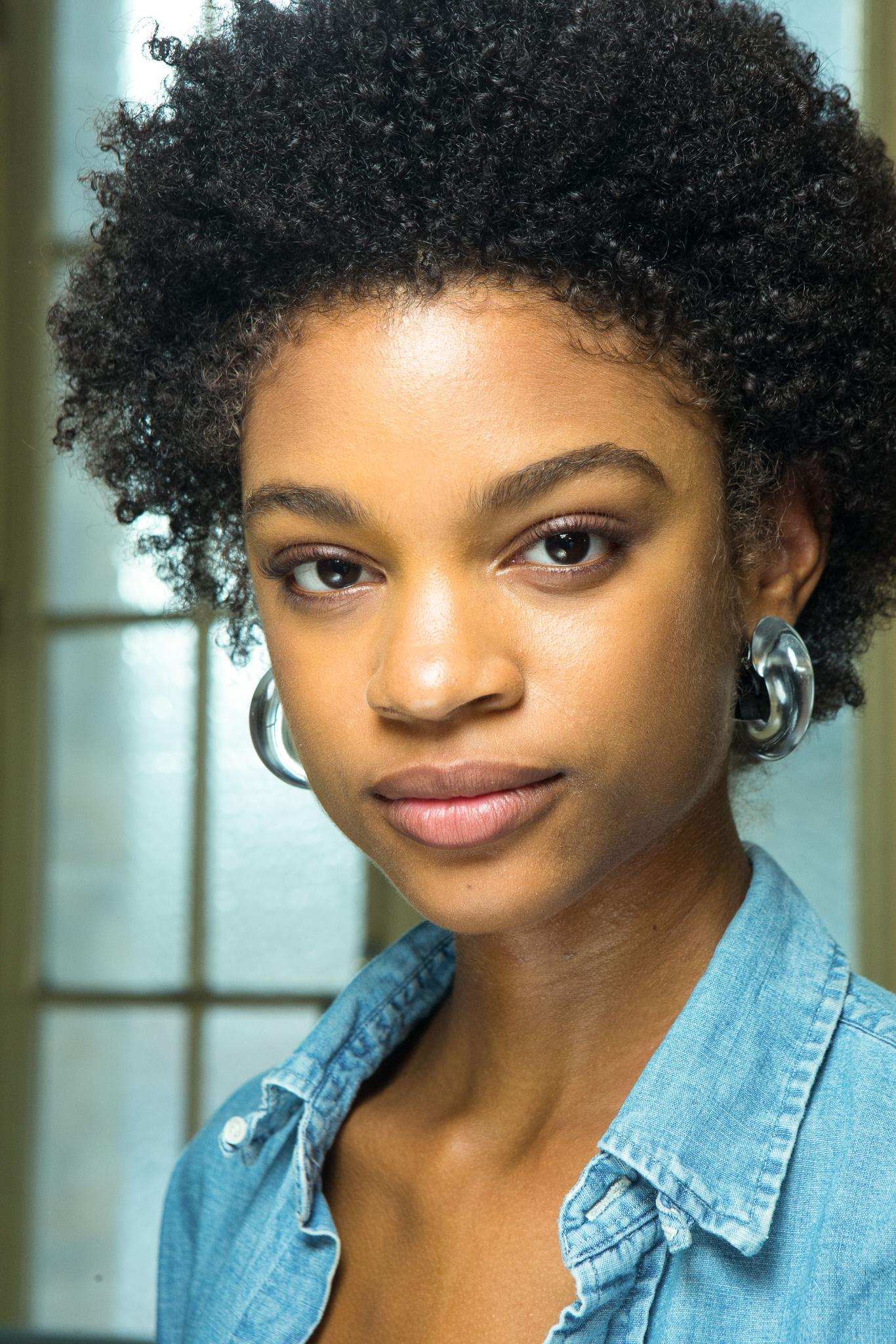 backstage shot of model with curly hairstyle, wearing denim and earrings