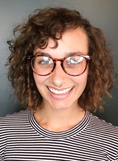 woman wearing glasses and a striped tshirt with shoulder length brunette hair in a curly perm