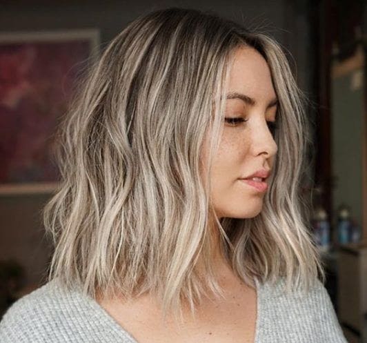 Shades of blonde hair: Woman with ash blonde highlighted wavy bob wearing a grey knitted jumper.