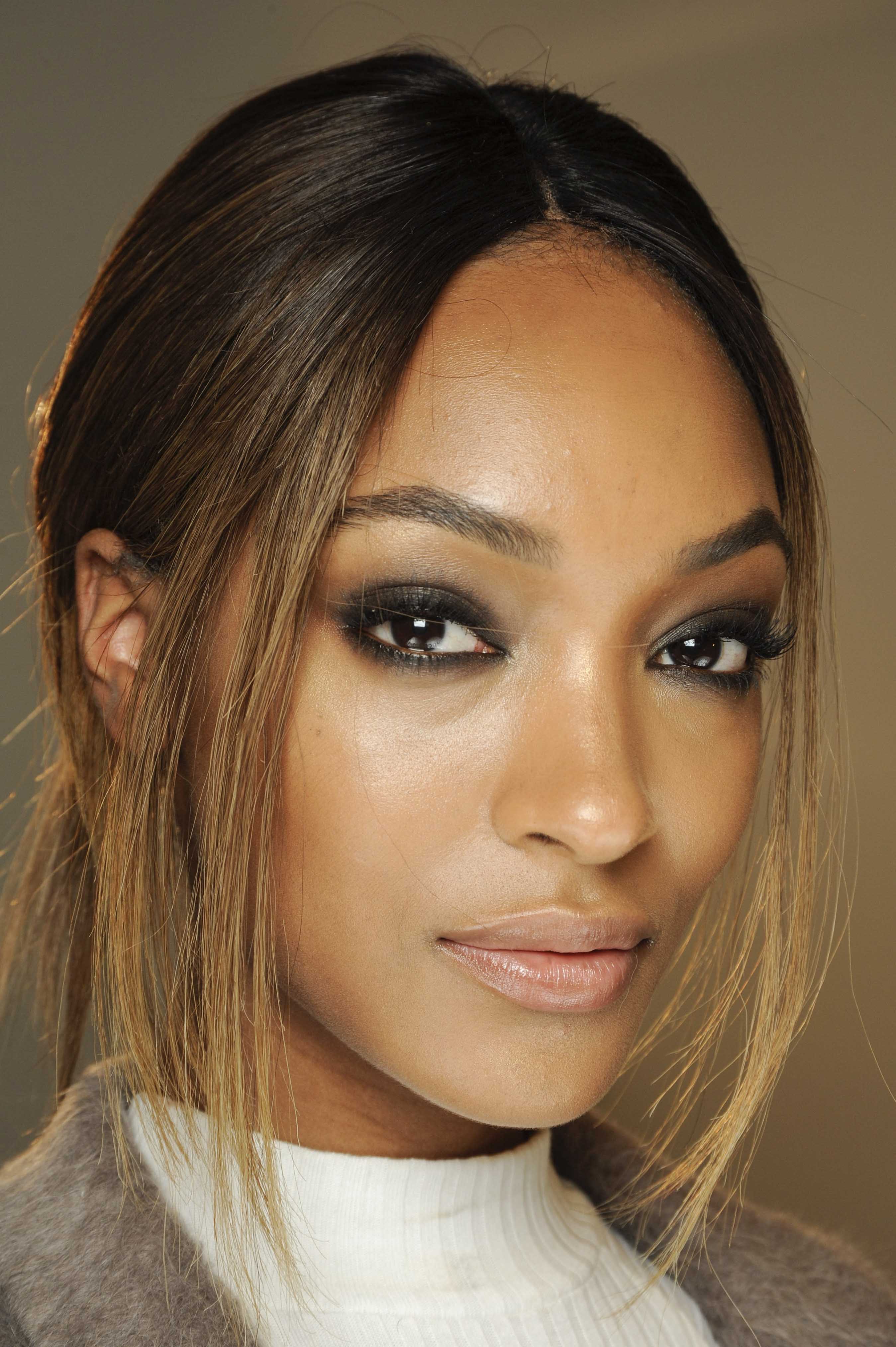 Balayage technique: Jourdan Dunn with dark golden brown balayage hair in low ponytail with dark eye make-up, and high neck top.