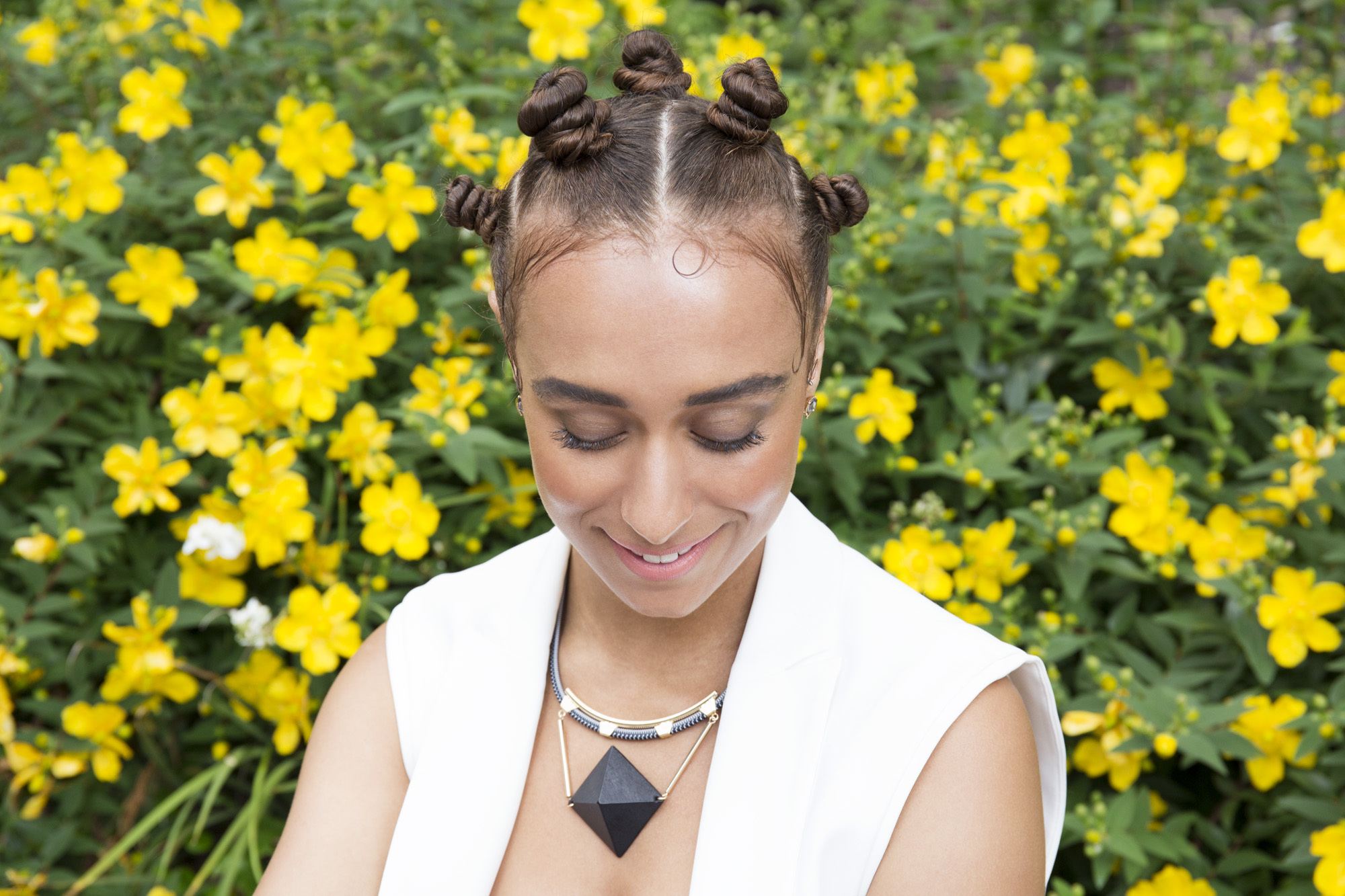 Low manipulation hairstyles: Close up shot of women with bantu knot hairstyle posing in a field of yellow flowers