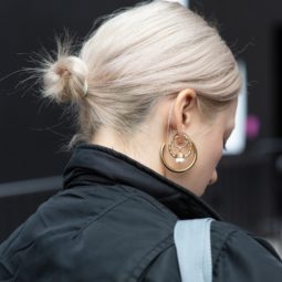 Woman with short bleached blonde hair styled into a low bun, wearing black jacket with hoop earrings on the street